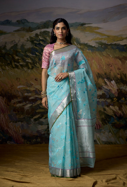 Luxury pastel blue handwoven Kota saree with silver zari cherry blossom jaal, gold zari accents, silver zari chevron pallu, minimal silver zari border with bright green selvedge and premium festive designer craftsmanship by Sonchiraiya