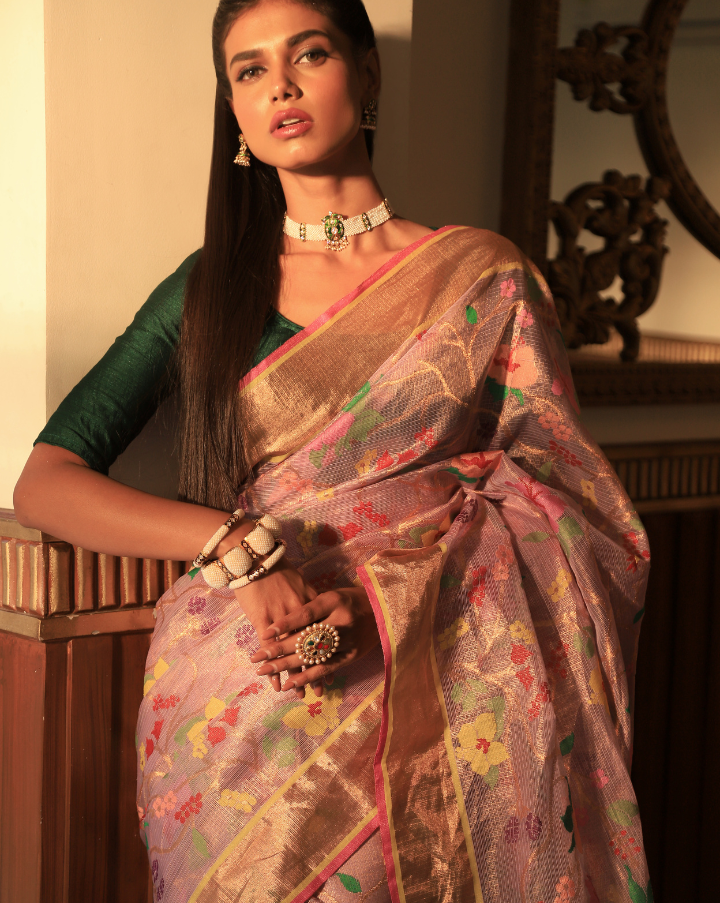 Woman wearing a handcrafted Lavender SónChiraiya zari Kota handloom saree with bright blooming hibiscuses and other bright flowers.