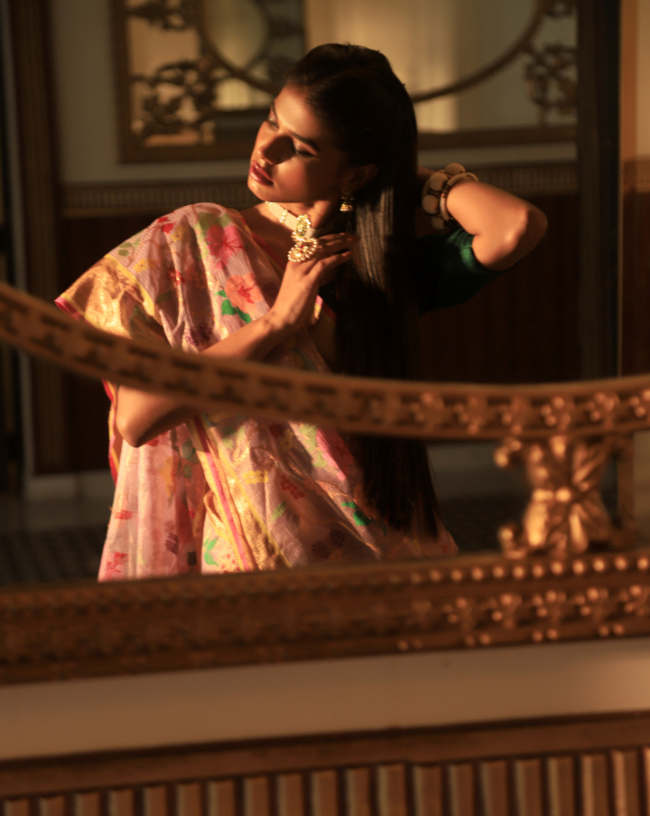 Woman wearing a handcrafted Lavender SónChiraiya zari Kota handloom saree with bright blooming hibiscuses and other bright flowers.