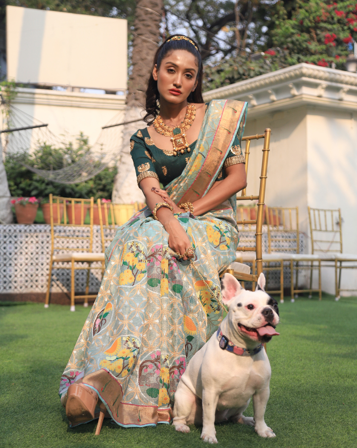 Woman wearing a light blue SónChiraiya zari Kota handloom saree, with a Muniya border, colourful birds and geometric floral motifs.