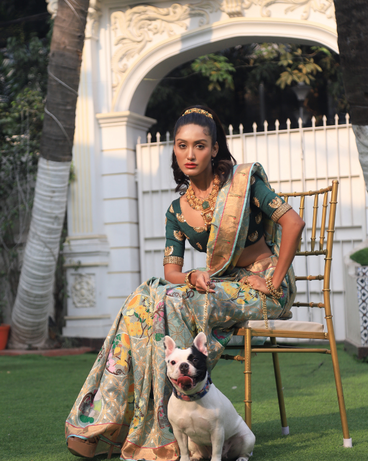 Woman wearing a light blue SónChiraiya zari Kota handloom saree, with a Muniya border, colourful birds and geometric floral motifs.