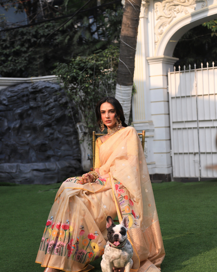 Woman wearing a beige SónChiraiya zari Kota handloom saree, with blooming vibrant flowers, gold and silver zari polka dots and a gold zari border.  