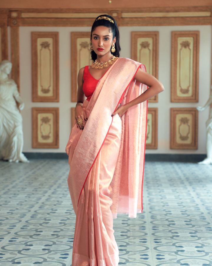 Woman wearing a light pink SónChiraiya Kota silk handloom saree with patterns in gold zari and wide borders featuring peacock and abstract motifs.
