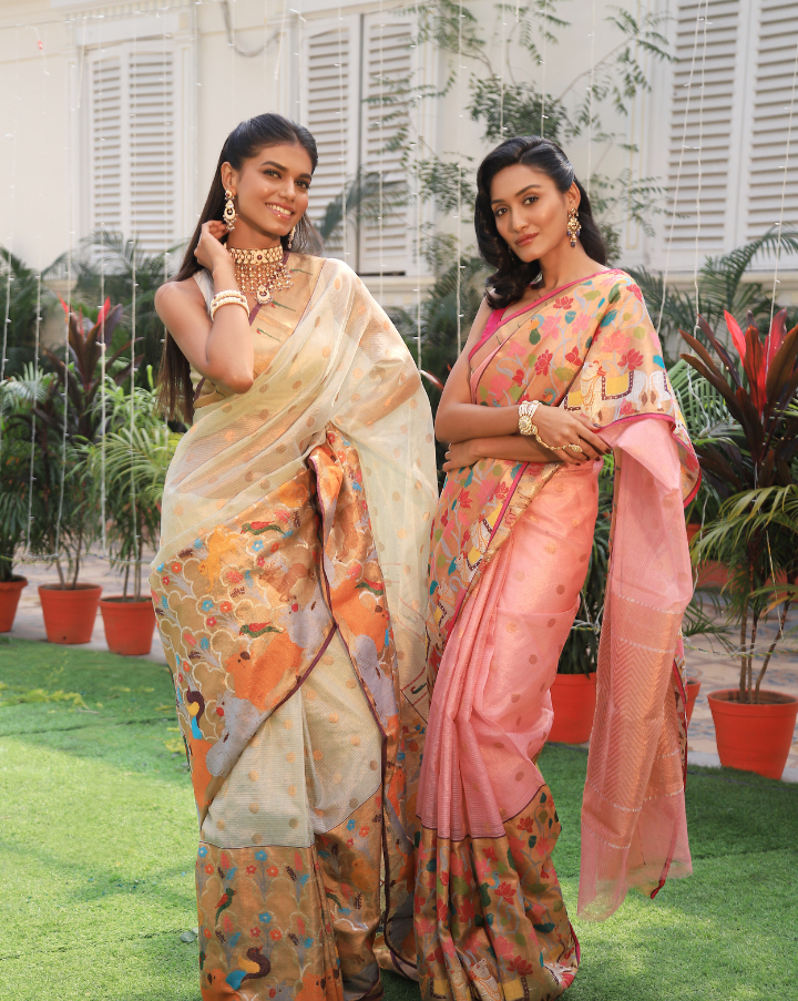 Woman wearing an off-white SónChiraiya zari Kota handloom saree with polka dots in gold zari, a classic Muniya border, and a wide border with various flora and fauna motifs.