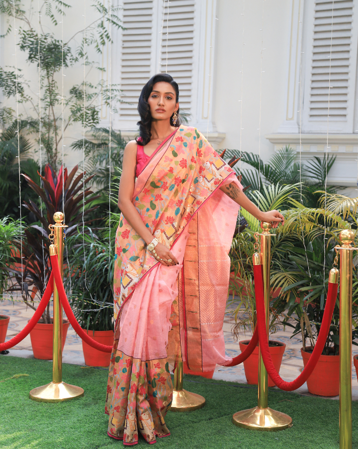 Woman wearing a light pink SónChiraiya zari Kota handloom saree with gold polka dots, Muniya border, and floral and animal motifs in Pichwai art.