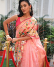 Woman wearing a light pink SónChiraiya zari Kota handloom saree with gold polka dots, Muniya border, and floral and animal motifs in Pichwai art.