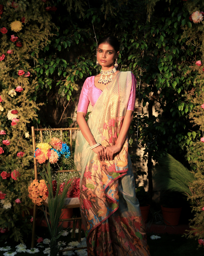 Woman wearing a light blue SónChiraiya Kota silk handloom saree with duck, fish, lotus and other floral motifs with gold and silver zari buttis.