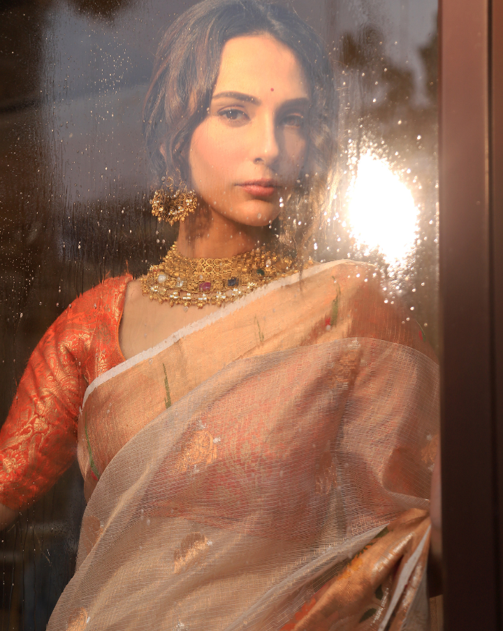Woman wearing an off-white SónChiraiya zari Kota handloom saree with silver and gold zari buttis, a simple Muniya border, and a wide ornate floral border.  