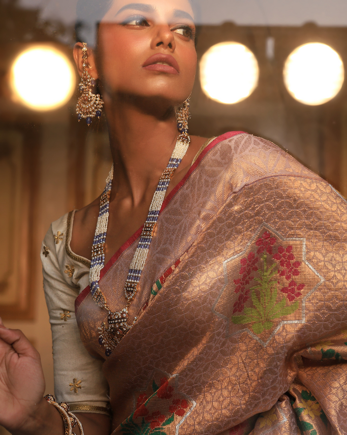 Woman wearing a blush pink SónChiraiya Kota silk handloom saree with geometric floral motifs in gold zari, and bright-hued bunches of flowers.
