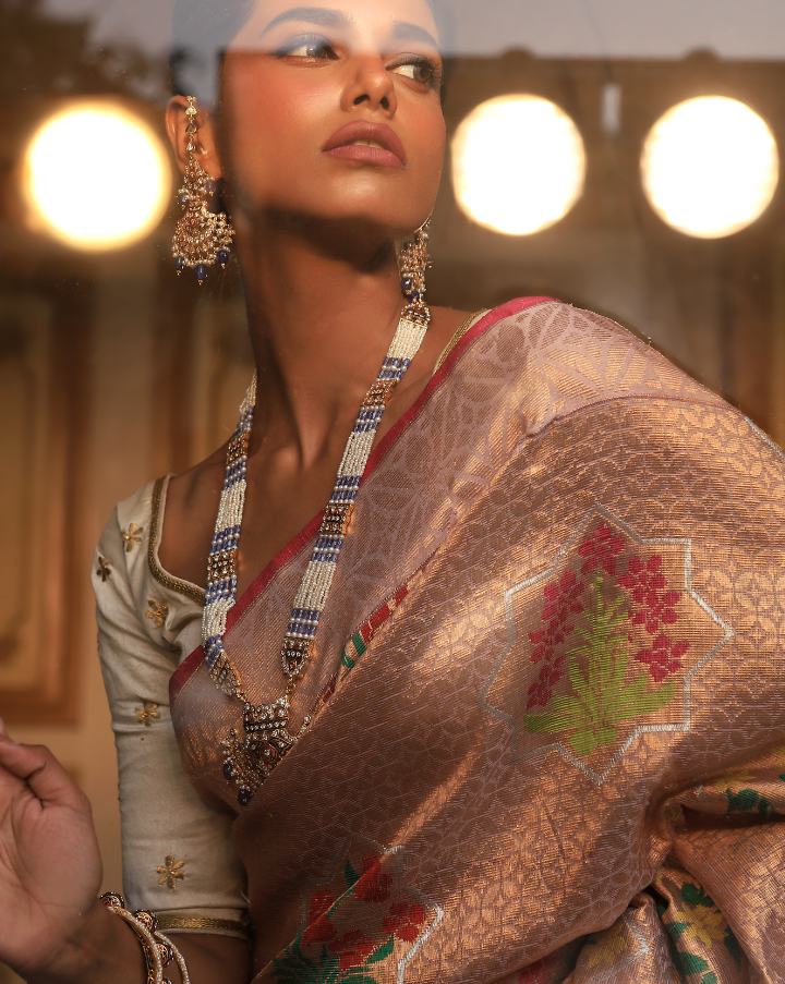 Woman wearing a blush pink SónChiraiya Kota silk handloom saree with geometric floral motifs in gold zari, and bright-hued bunches of flowers.