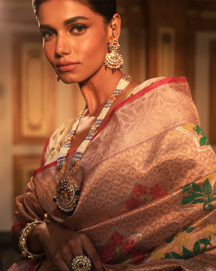 Woman wearing a blush pink SónChiraiya Kota silk handloom saree with geometric floral motifs in gold zari, and bright-hued bunches of flowers.
