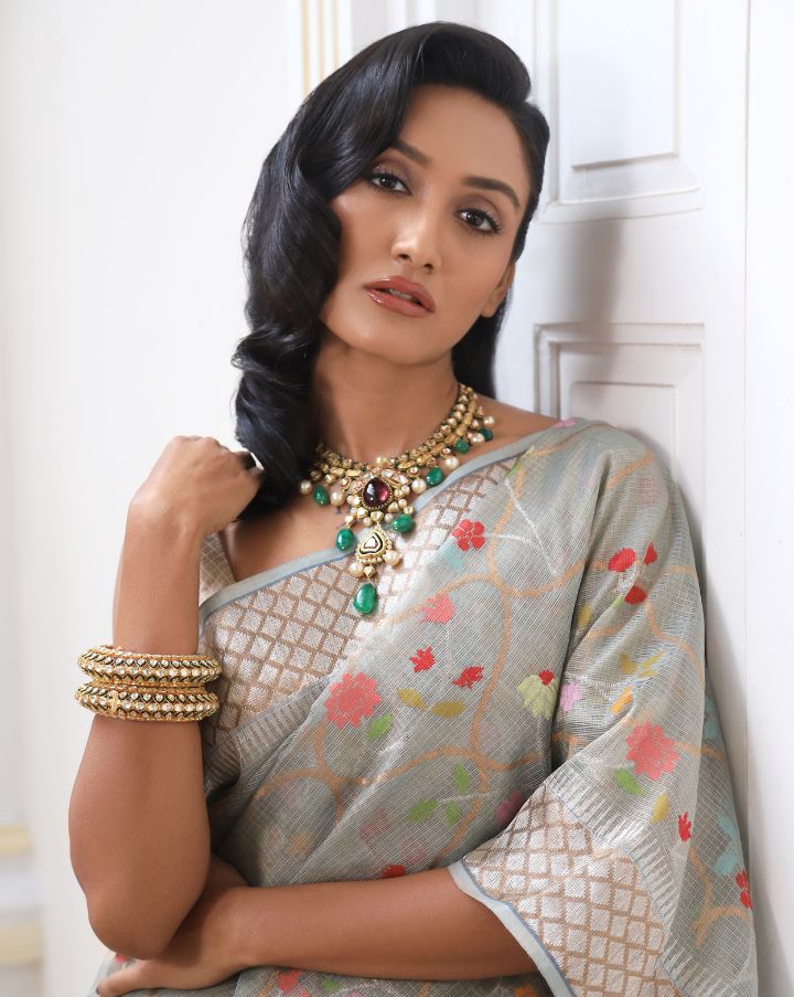 Woman wearing a grey SónChiraiya zari Kota handloom saree with colourful flowers, gold and silver zari accents and ornate borders.