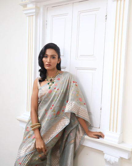 Woman wearing a grey SónChiraiya zari Kota handloom saree with colourful flowers, gold and silver zari accents and ornate borders.