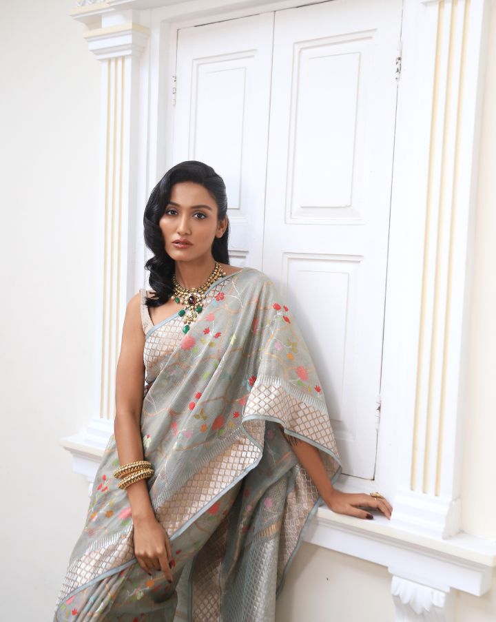 Woman wearing a grey SónChiraiya zari Kota handloom saree with colourful flowers, gold and silver zari accents and ornate borders.