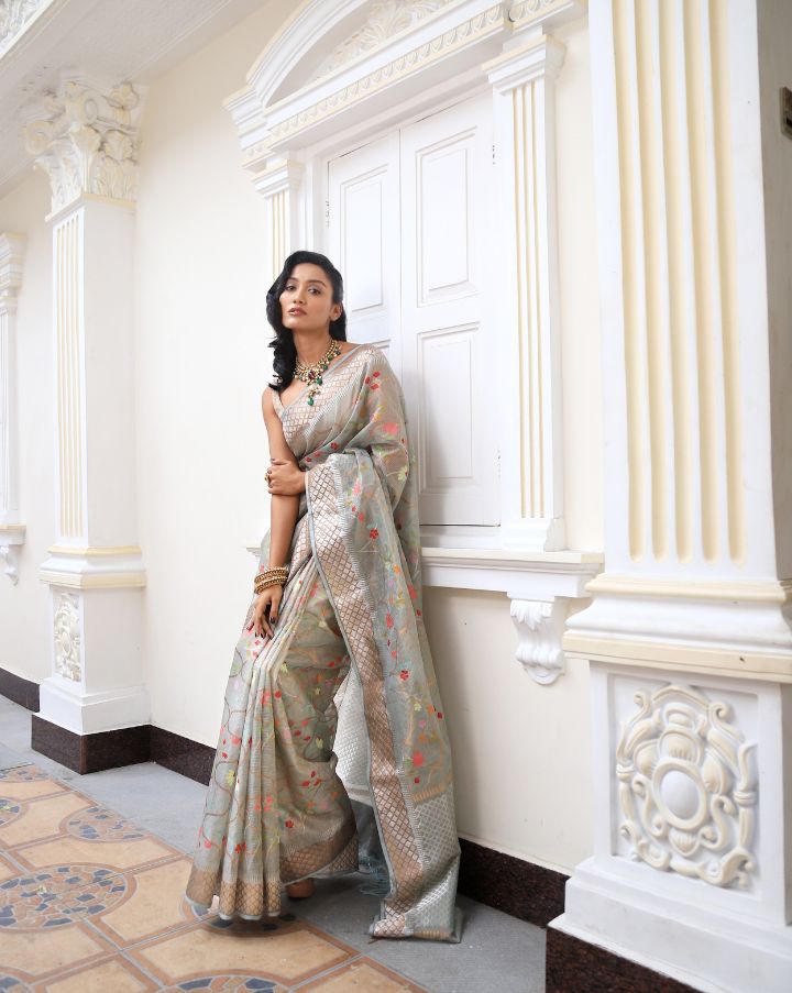 Woman wearing a grey SónChiraiya zari Kota handloom saree with colourful flowers, gold and silver zari accents and ornate borders.