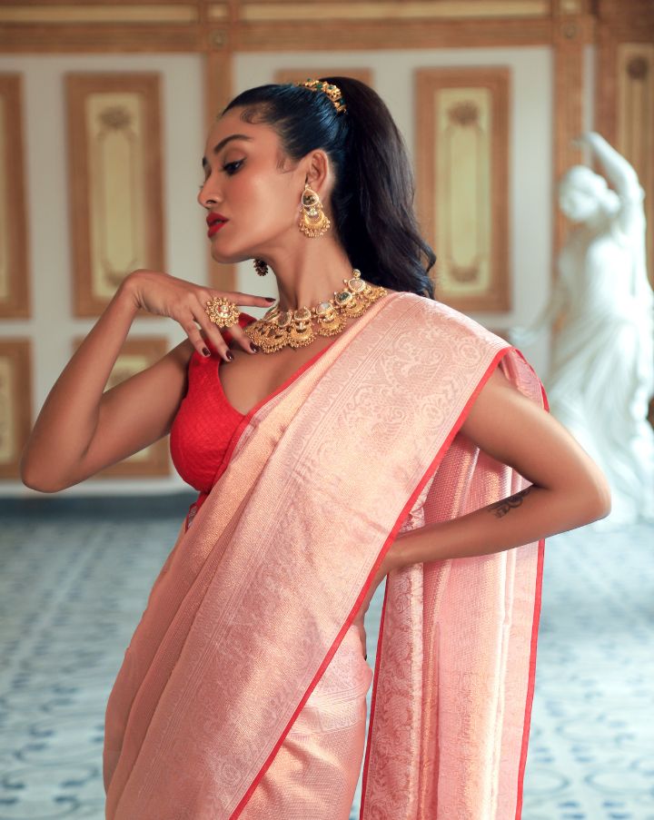 Woman wearing a light pink SónChiraiya Kota silk handloom saree with patterns in gold zari and wide borders featuring peacock and abstract motifs.