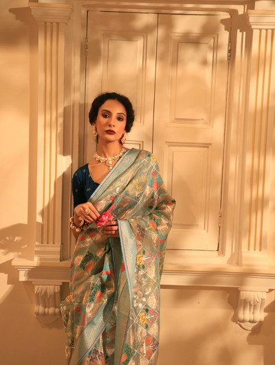 Woman wearing a light blue SónChiraiya zari Kota handloom saree with bright flora and fauna motifs, and real gold and silver zari florals encased within geometric patterns.  