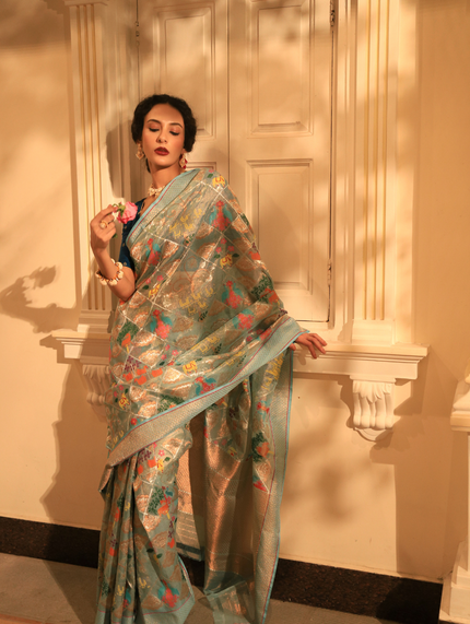 Woman wearing a light blue SónChiraiya zari Kota handloom saree with bright flora and fauna motifs, and real gold and silver zari florals encased within geometric patterns.  
